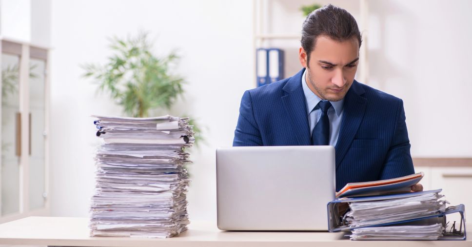 Homem cheio de arquivos físicos. Entenda mais sobre como fazer a redução do uso de papel com a digitalização!
